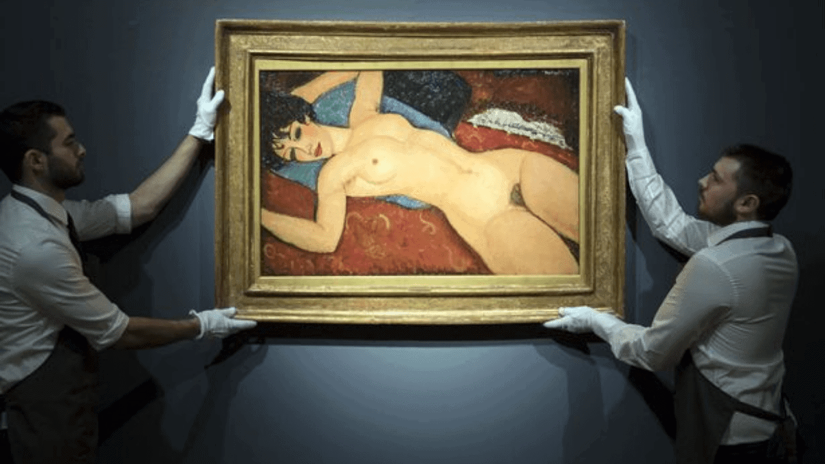 The painting Nu couché by Amedeo Modigliani held by two men at an auction. 