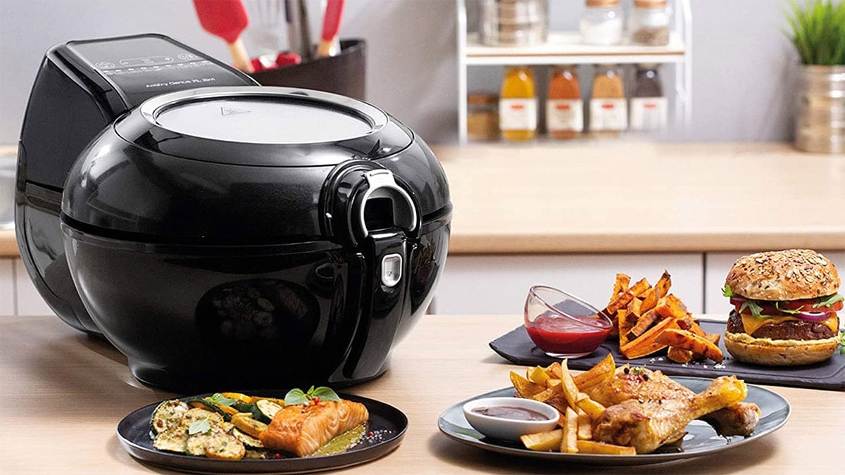 A black air fryer on a table. beside it is fried food made with the air fryer. 