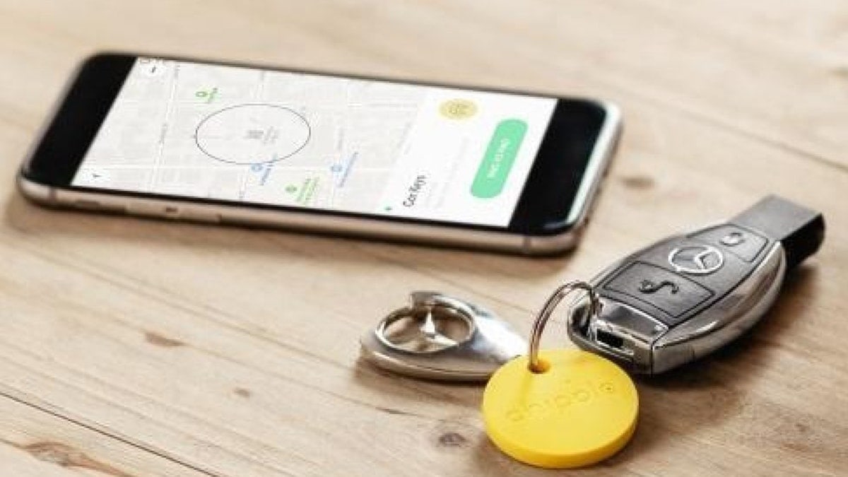 A Bluetooth tracker attached to car keys. Beside it is a phone with the tracker app. 