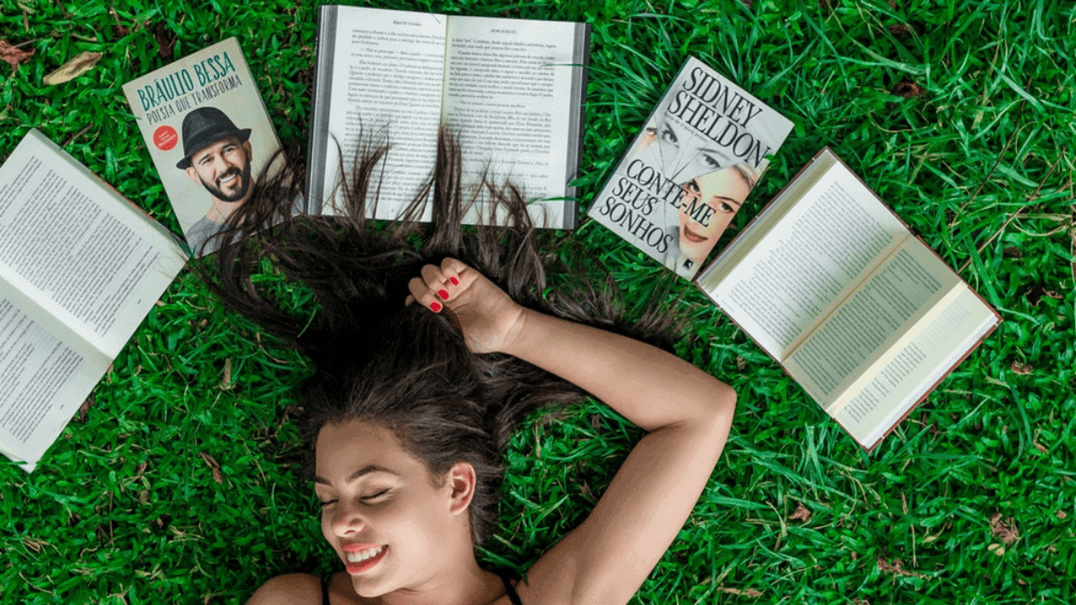 A girl lying in the garden and there are books over her head. 