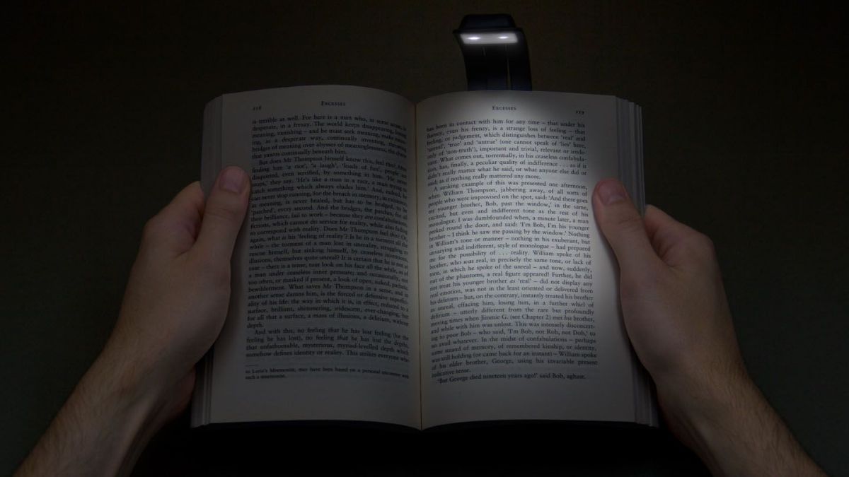 a person reading a book in darkness with the help of booklight.