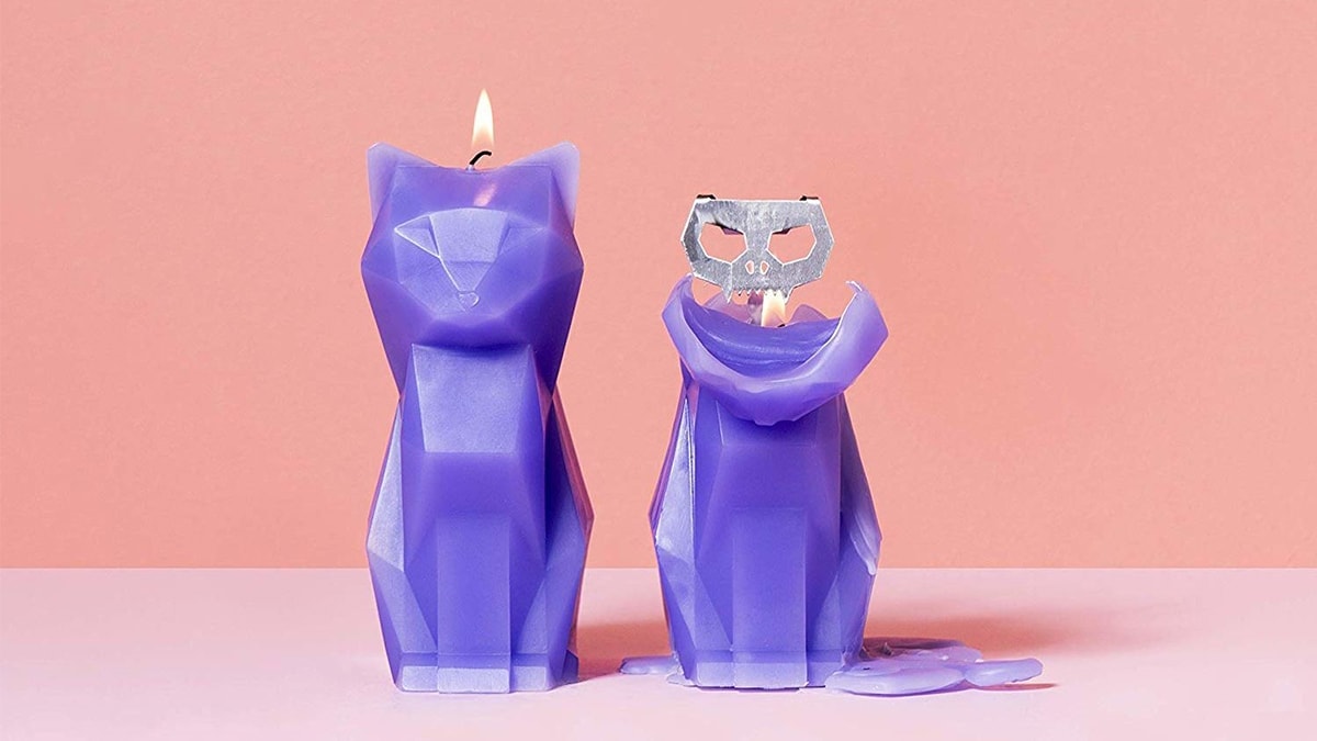 a purple colored burning Cat shaped candle on the left side and a metallic skeleton being exposed on the right side on a pink background.