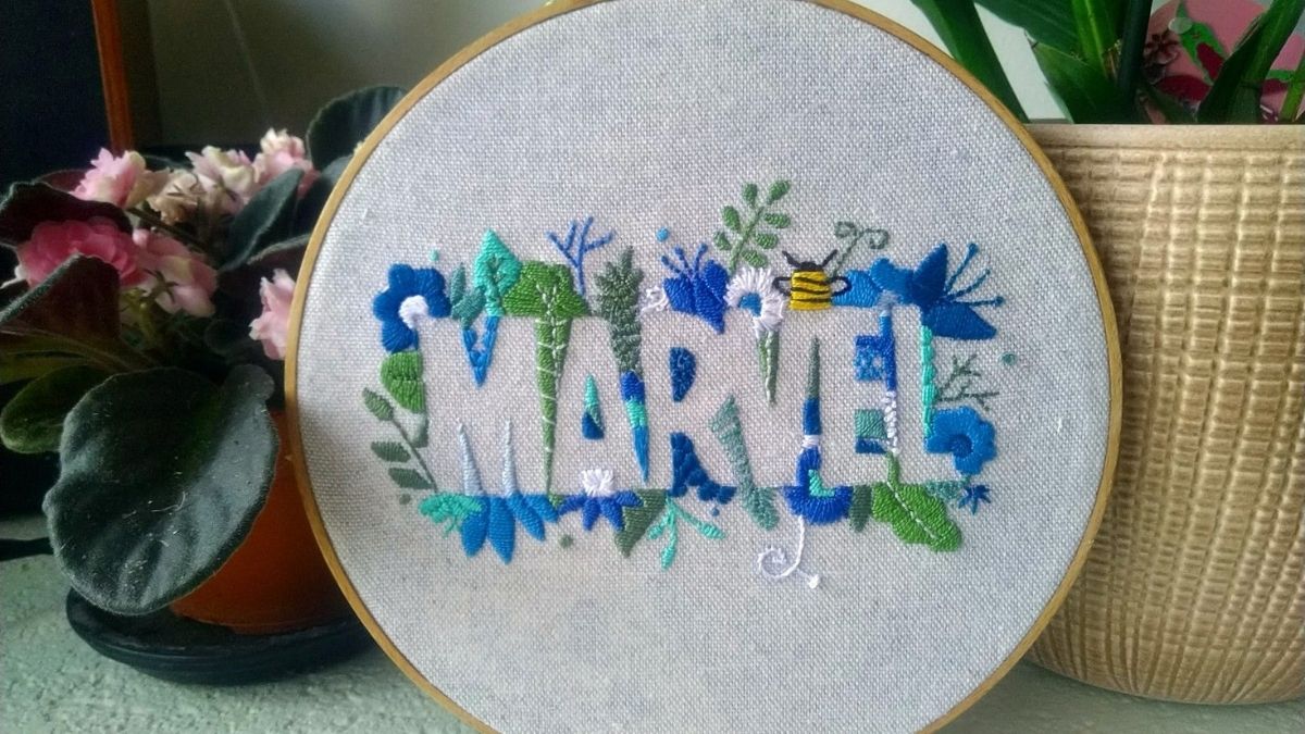 A embroidery marvel hoop art is placed beside the artificial plant in the living area. 