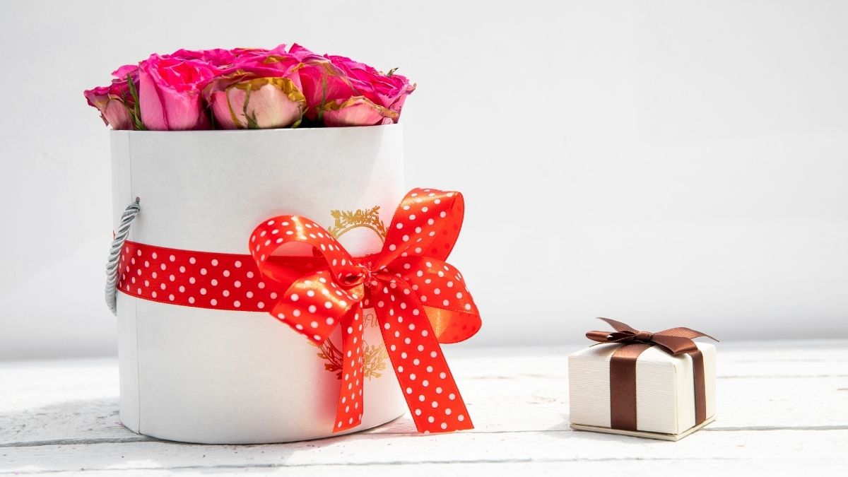 A flower bouquet is kept besides a tiny gift box on a white background. 