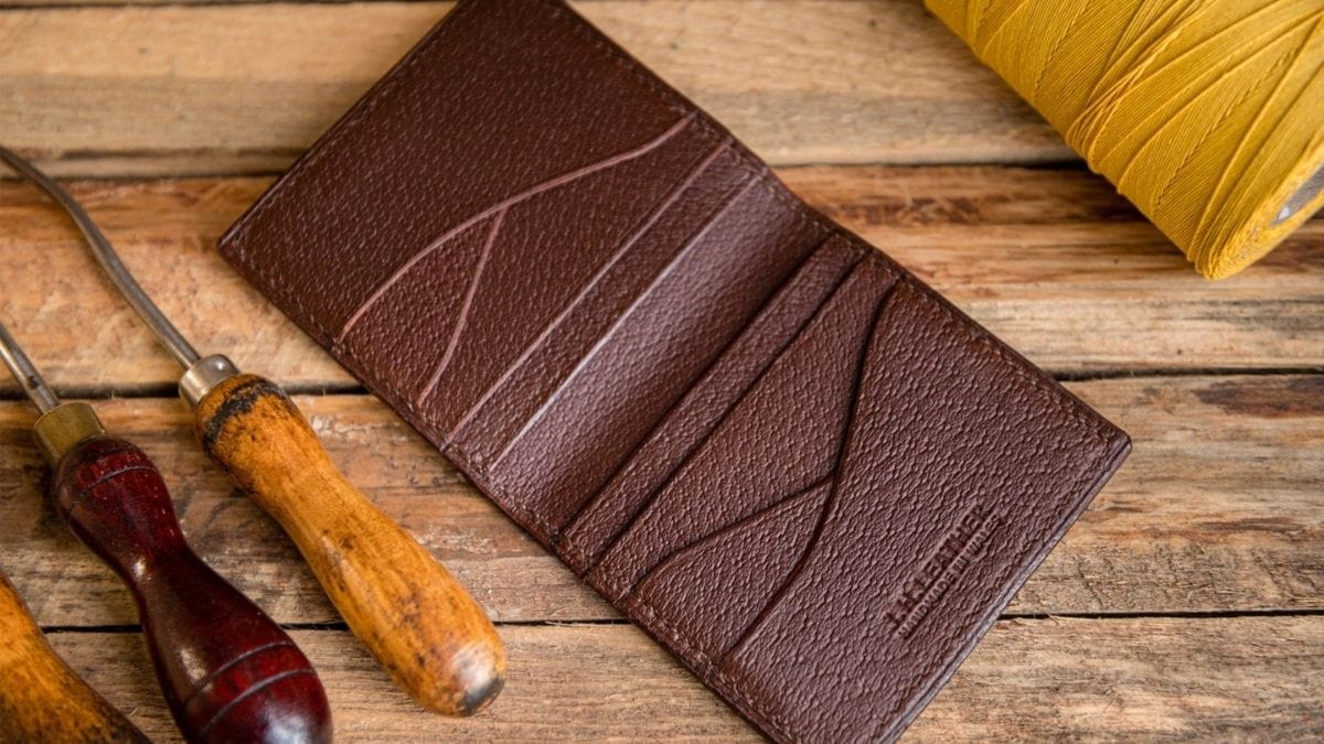 A brown colored leather wallet is placed on a wooden surface. 