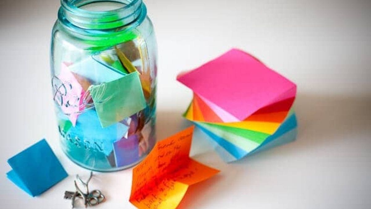 A memory jar filled with letters, sticky notes, and chocolates is placed on a white surface. 