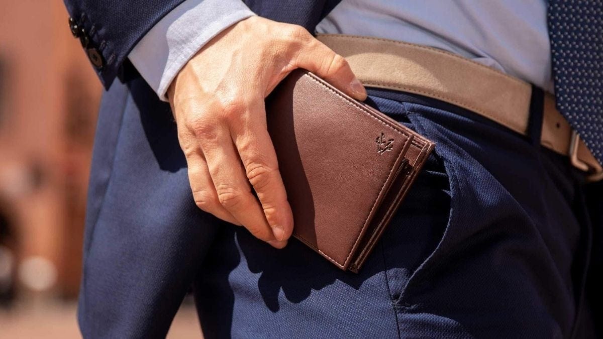 A man wearing formals putting a brown wallet into his pocket. 