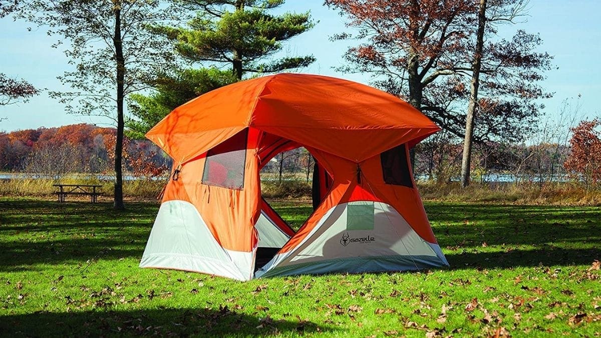 An orange portable camping tent is set outside in the wild. 