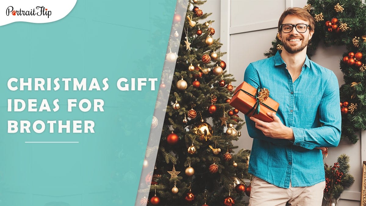 Christmas gift ideas for brother: a man in a blue shirt hold a christmas gift as he poses beside a christmas tree. 