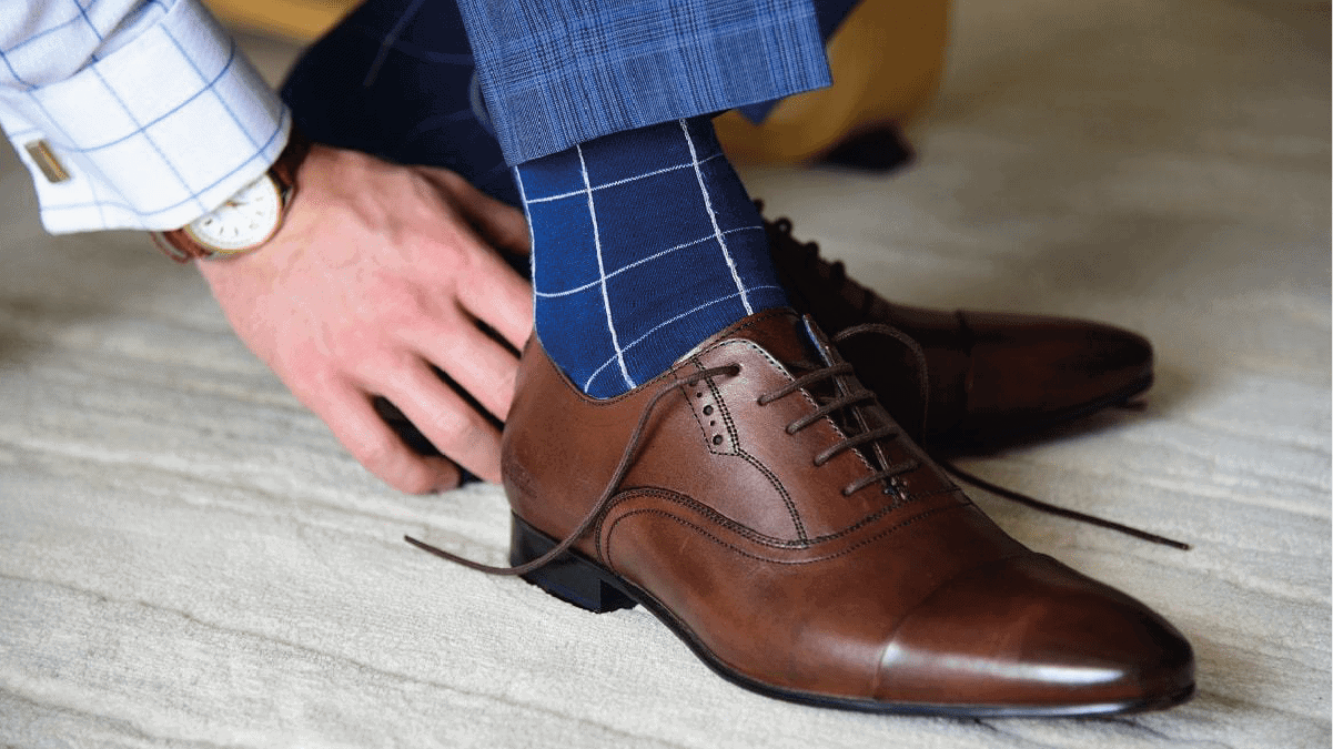 A guy wearing blue socks is tying the lace of brown shoes