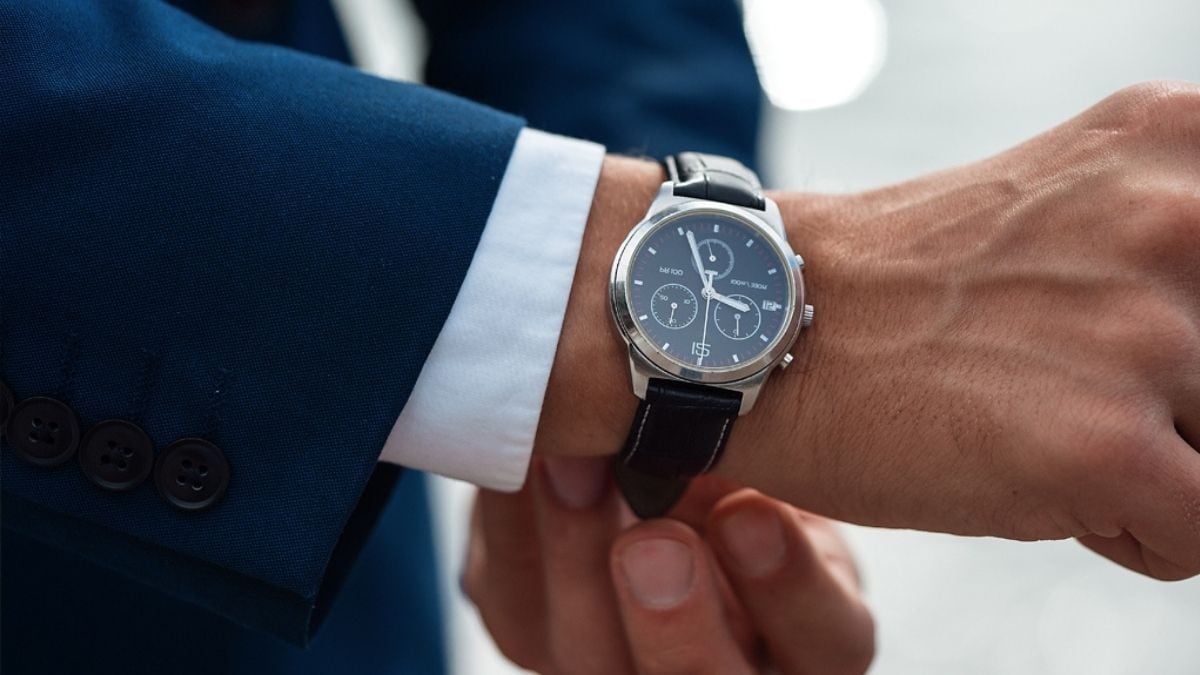 A man in formals showing his timepiece. 