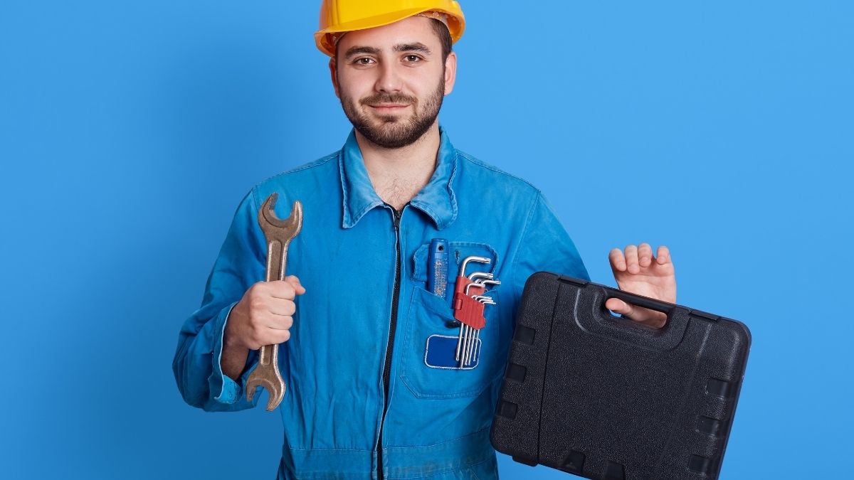 A man is smirking by holding a tool bag in his finger on a blue background. 