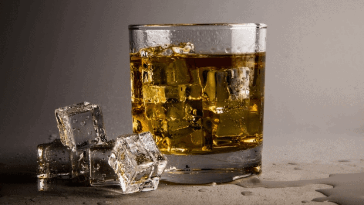 A classic whiskey glass is placed on the plain surface with three ice cubes on its sides. 