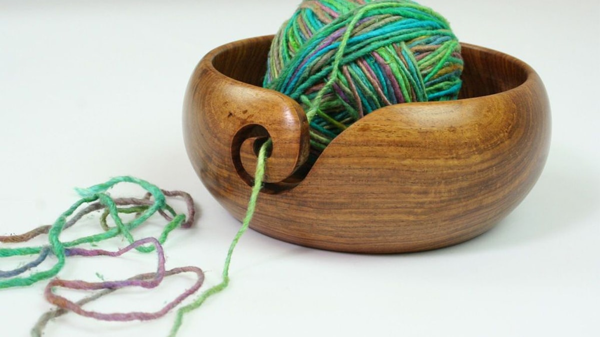 A brown yarn bowl with colorful green and blue yarn. 