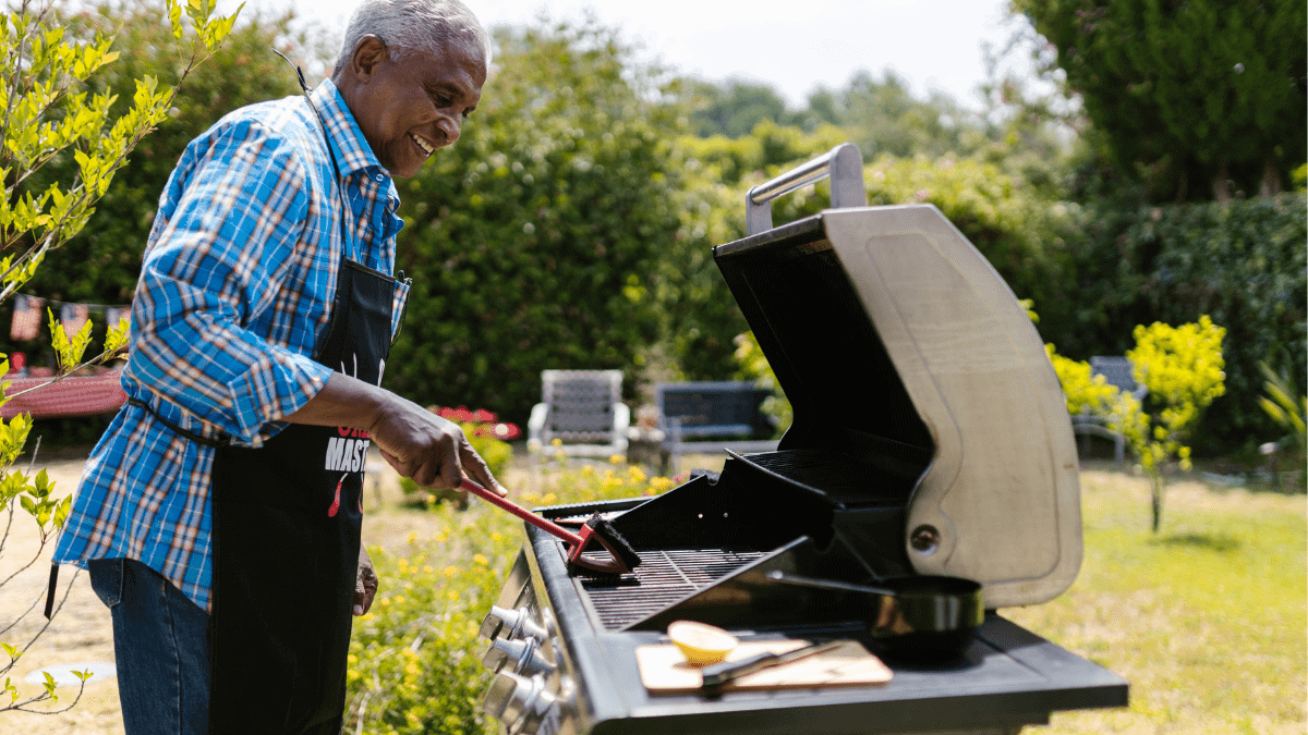An old man happily Barbequing in a garden. 