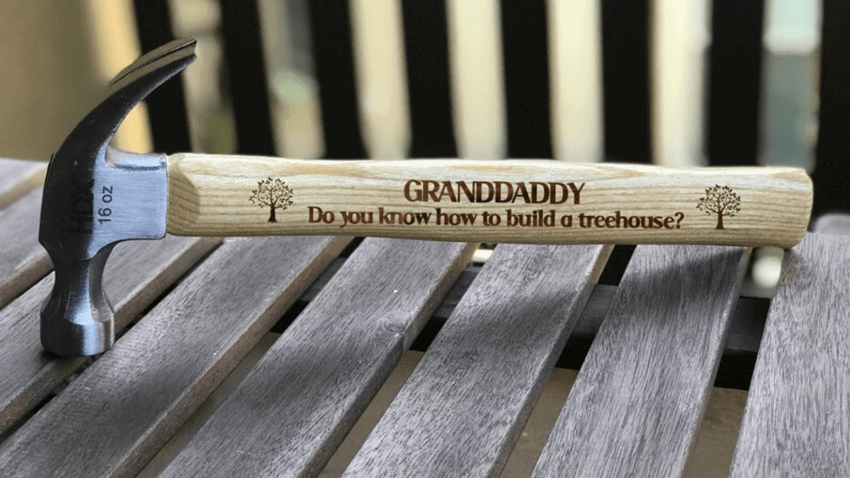 A personalized hammer, with brown wooden handle and metal front.
A message engraved for granddad on the wooden handle 
