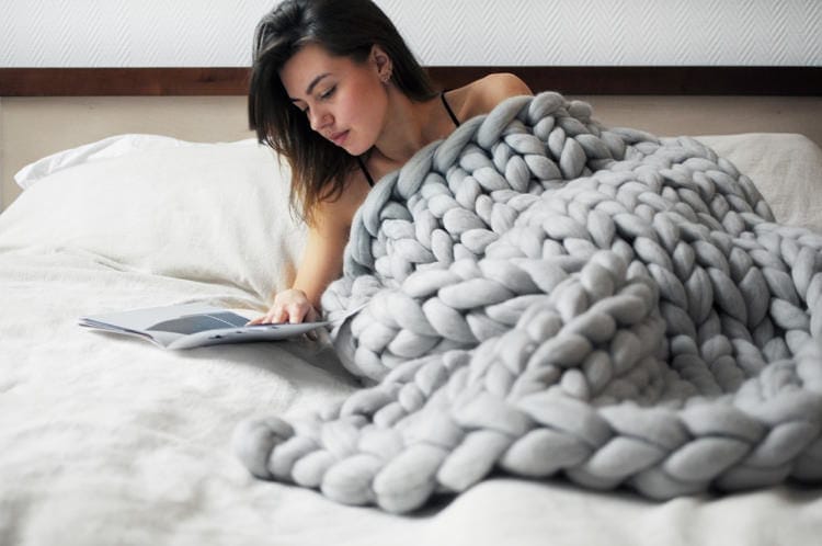 a woman checking her phone while being cozy with a large throw blanket