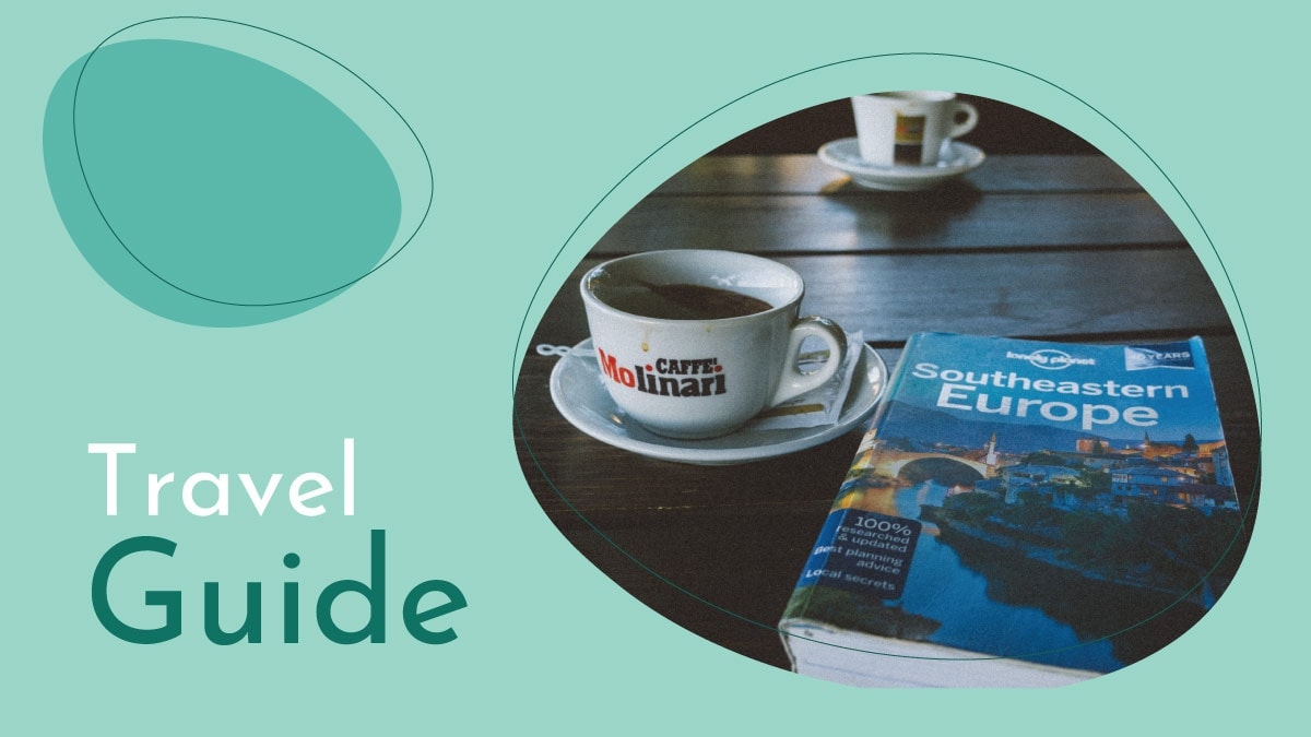 A travel guide is kept besides a cup of tea on the wooden bench. 