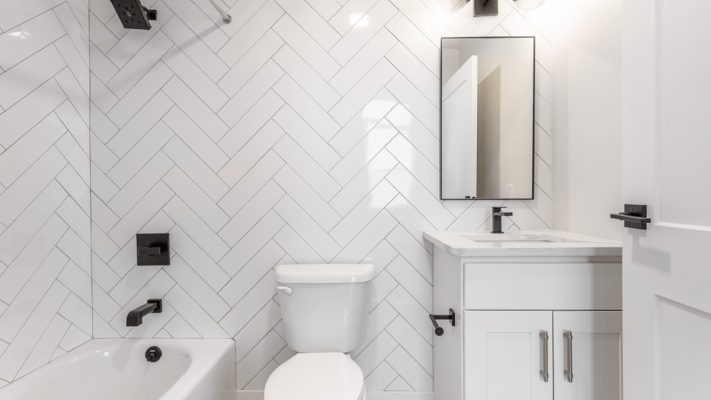 White colored tiles are installed on the walls of a bathroom. 