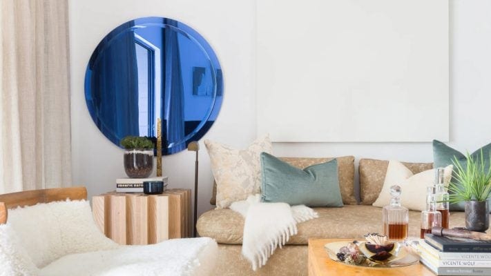 An iridescent mirror mounted on the plain white wall behind the sofa. 