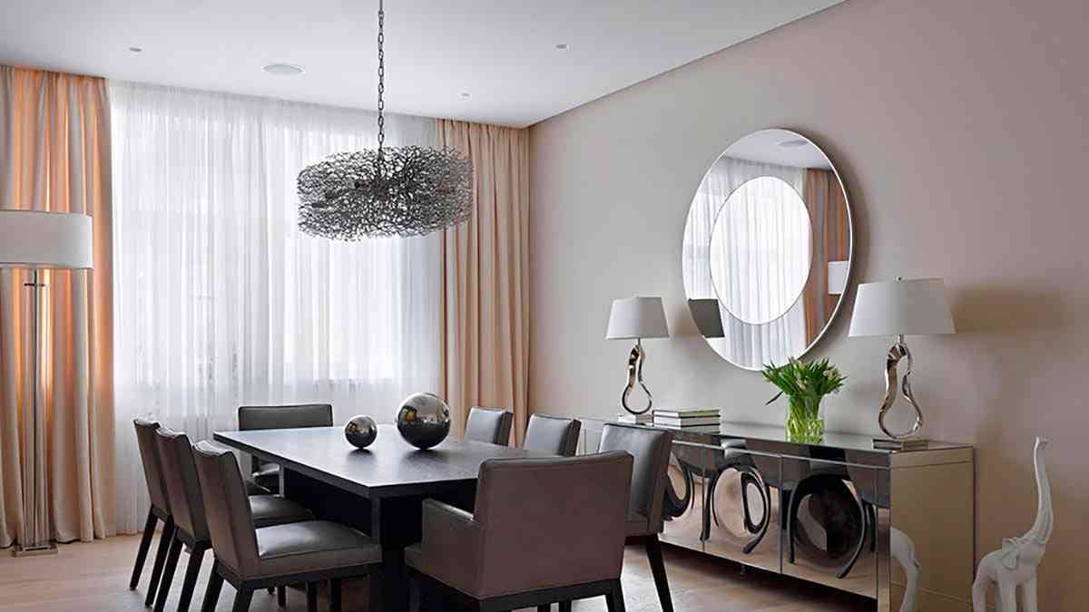 A round mirror is mounted on the wall of a dining room. 