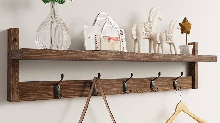 Wooden hooks are mounted on the plain white wall of a entryway. 