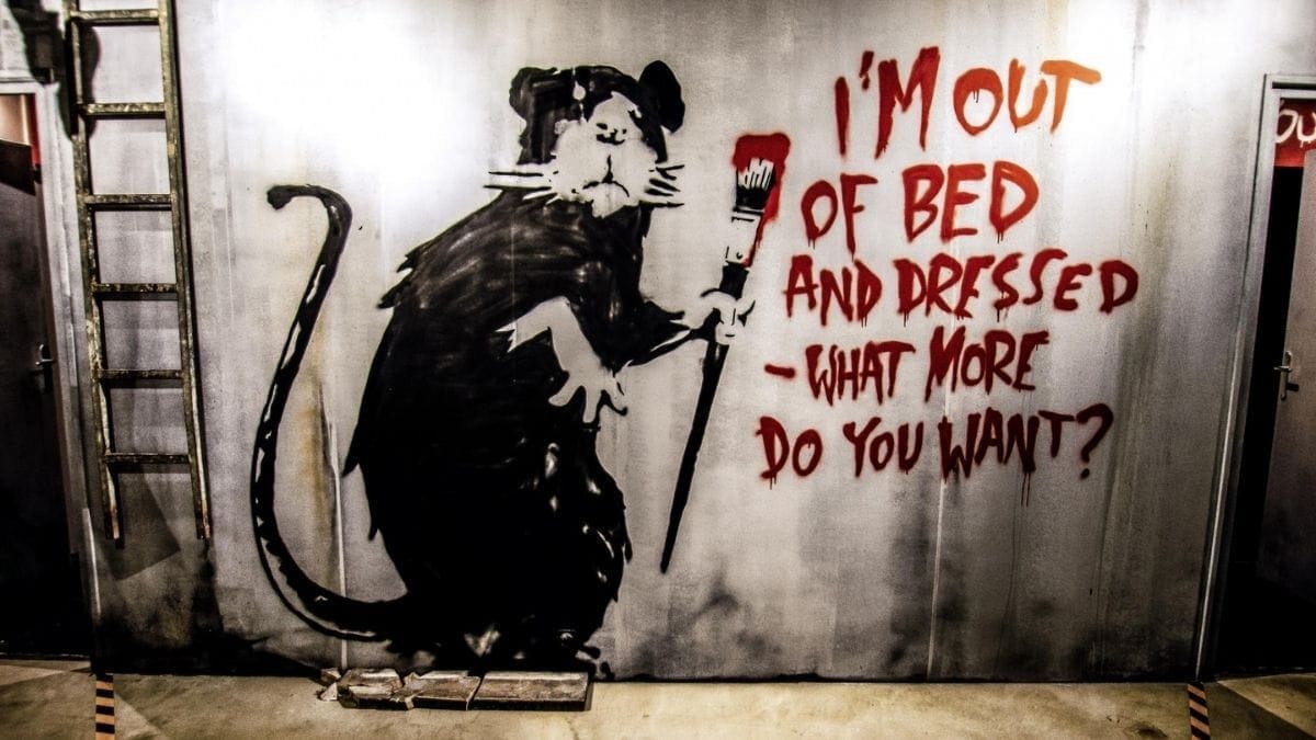 Banksy, a mysterious artist from England.
This graffiti depicts a mouse  who says "I'm out of bed and dressed - what more do you want? 
  
