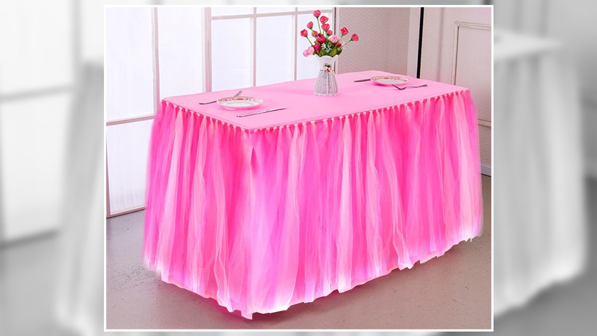 A tabletop decorated with a pink cloth, a flower pot with roses, and two plates. 