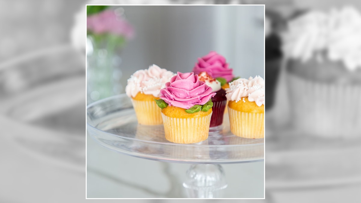 cupcakes with pink, and white cream toppings are kept in a glass tray.
