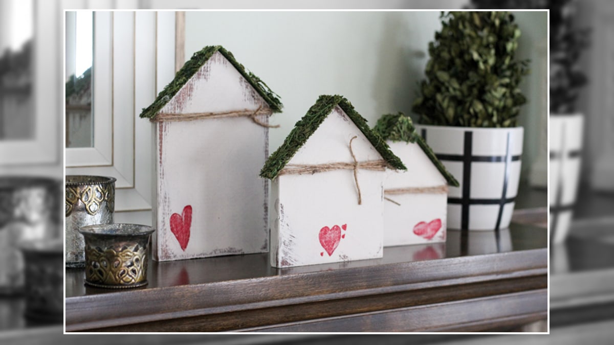 Three house shaped wooden decor items with pink heart on it are placed on a desk as an addition to the 14th February decor. 