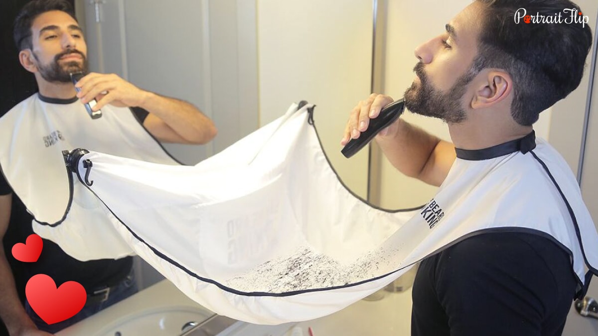 A man trimming his beard while wearing a beard bib. The trimmed beard is caught on the beard bib