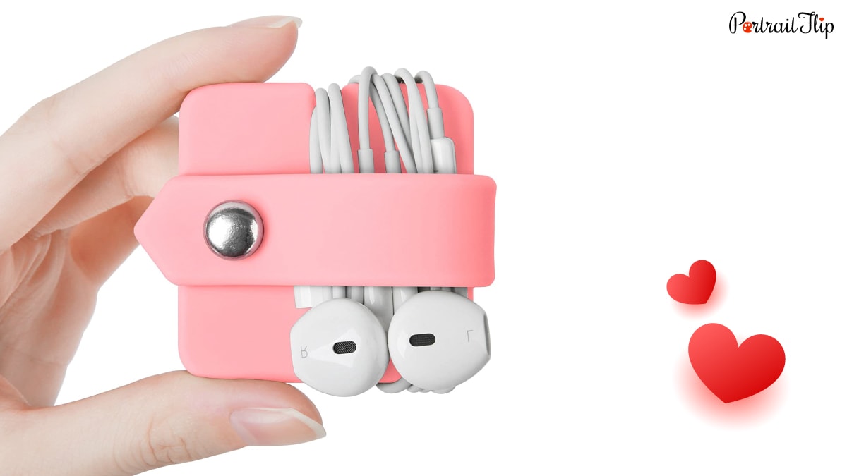 A hand holding an pink colored  earphone organizer with an earphone cable organized in it. 