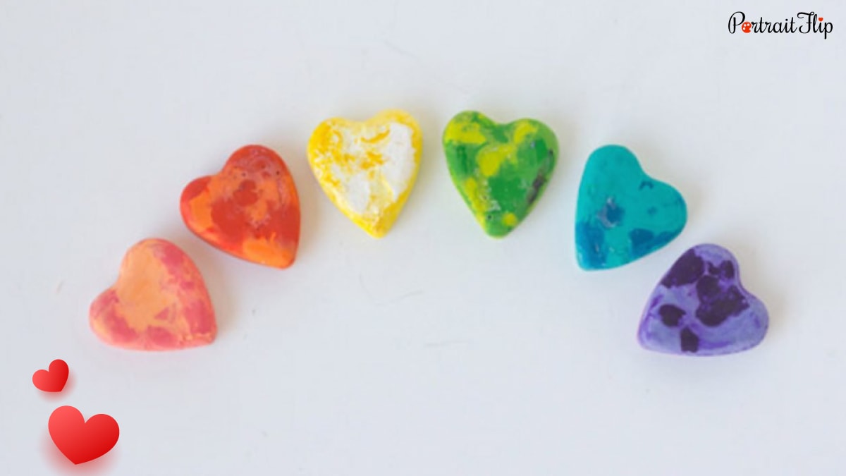 peach, orange, yellow, green, turquoise, purple colored heart crayons kept on a white surface