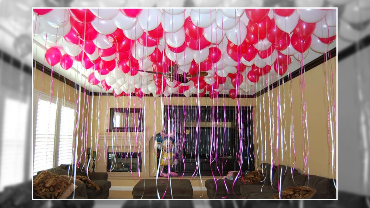 Pink and white balloons with ribbons filled in a room