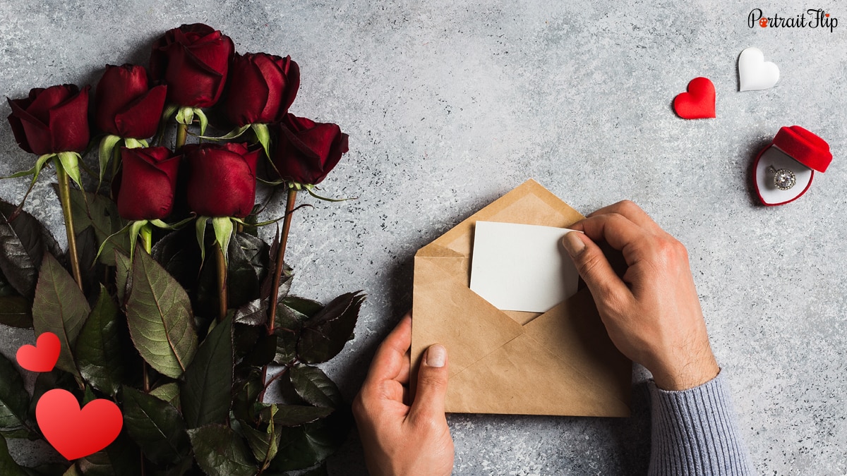  a man putting a letter in an envelope and beside it, is a rose bouquet. 