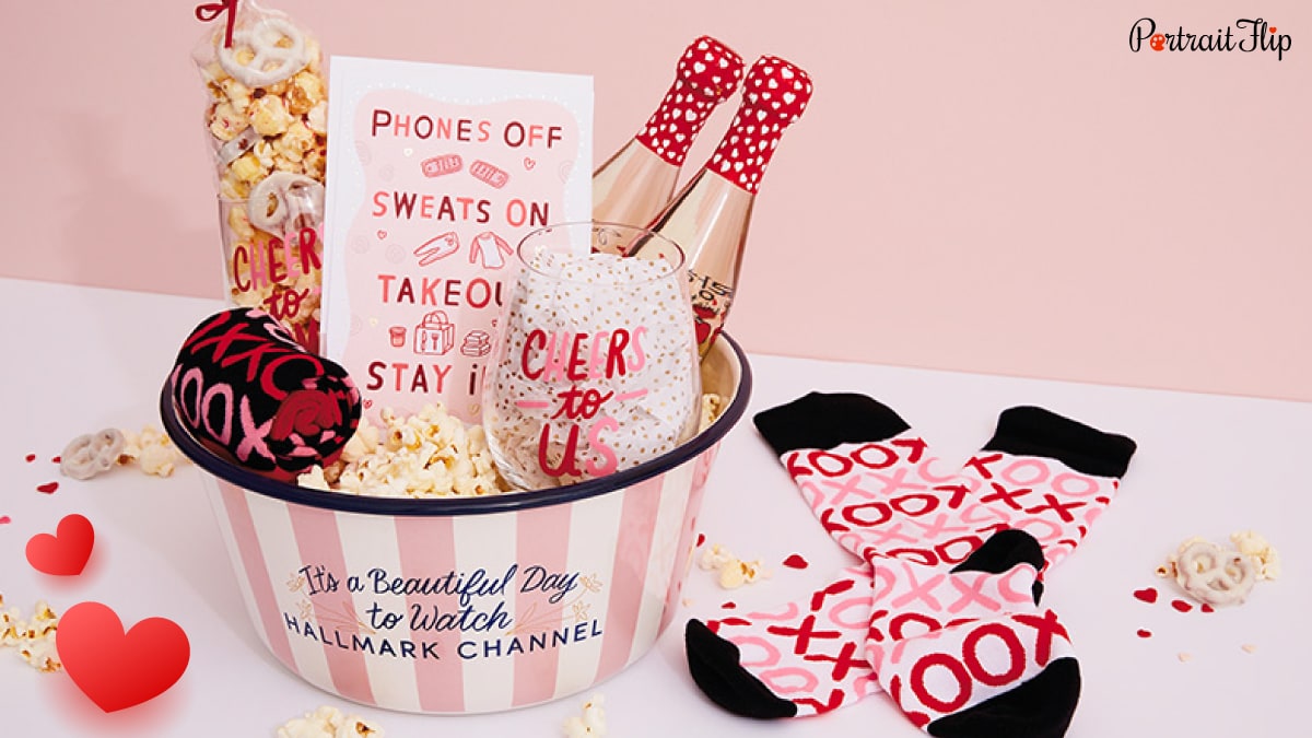A small valentine's day themed bucket that has socks, champagne bottles,  valentine's day card, and popcorn. 