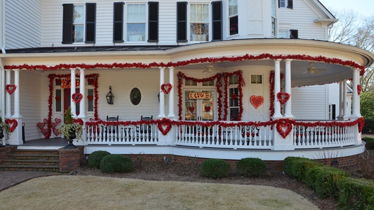 A white porch is decorated with red garland s and wreaths. 