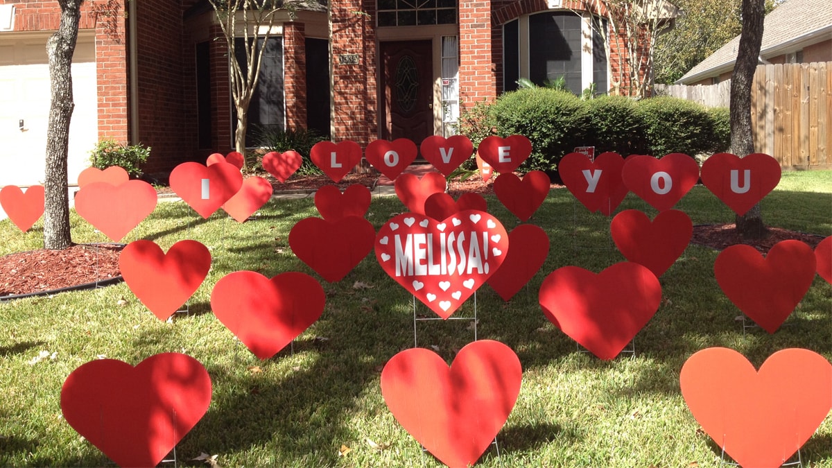 The outside of house- a yard is decorated with big hearts that spell "I Love You, Melissa!" 