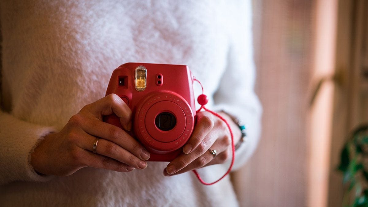 A girl holding a red polaroid camera in her hand.