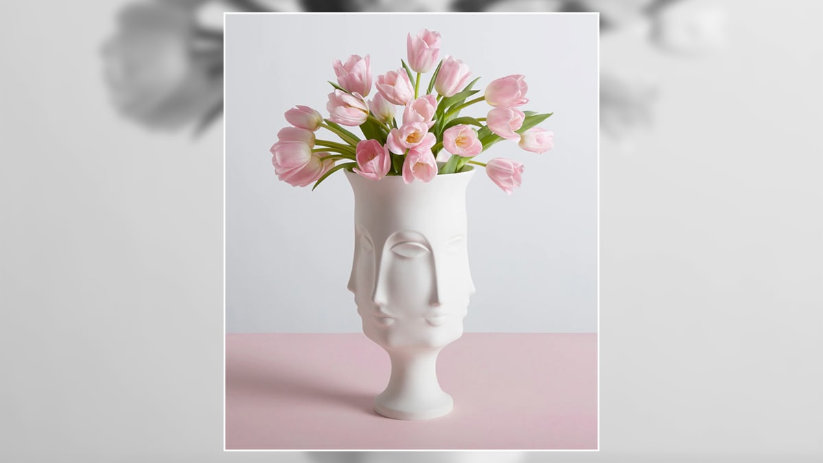 a white  woman face shaped flower pot with pink roses. 