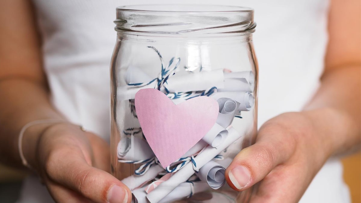 A person holding a mason jar full of small chits which have reasons why you love them written in them.