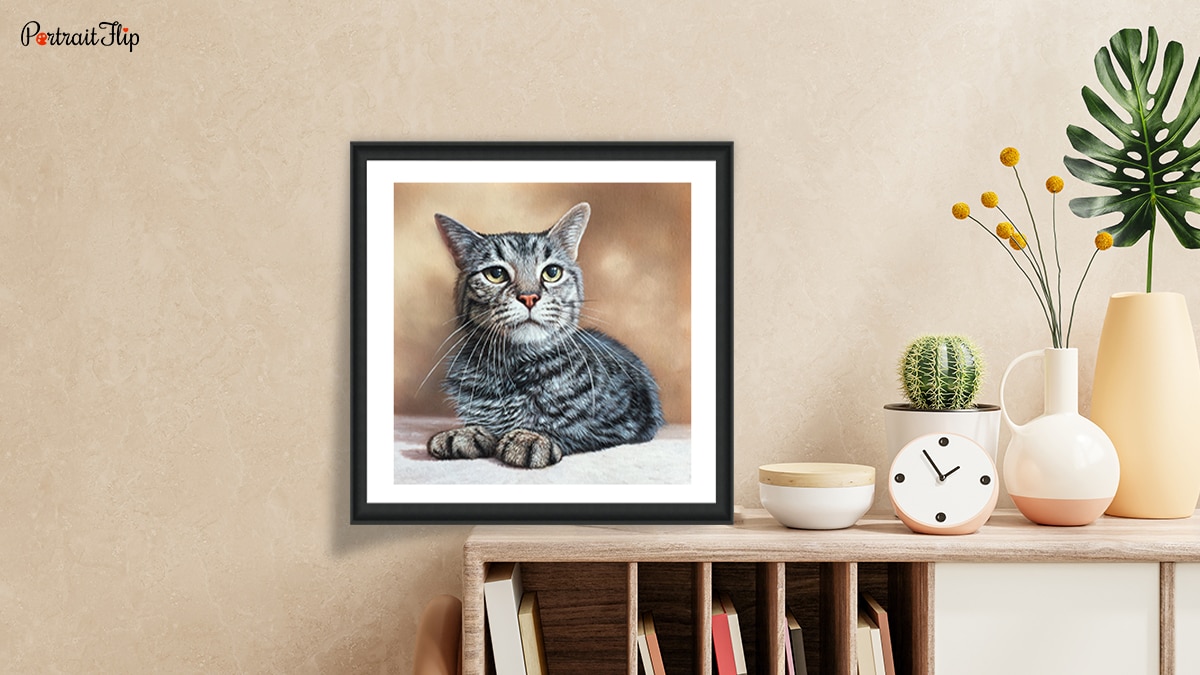 A portrait of a cat sitting on a table with home decorations surrounding it.
