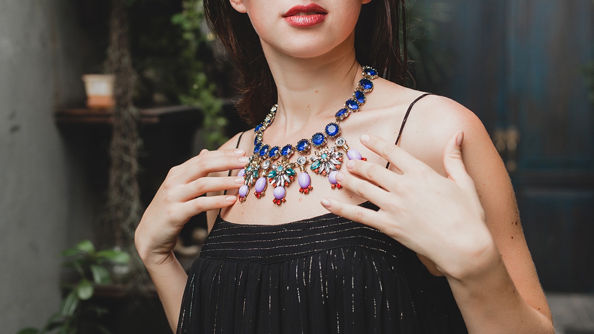 a woman in black dress showing off her   vibrant jewel necklace. 