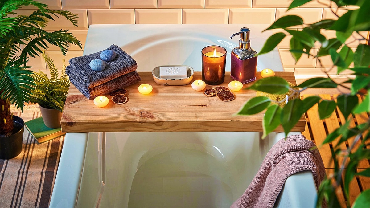 a wooden bathtub caddy with candles, towels, bath bombs, soap, shampoo is kept on  a bathtub. 