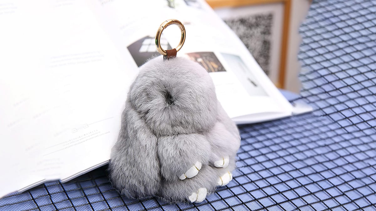 A rabbit keychain that is furry and grey. It is a gift for rabbit pet lovers.