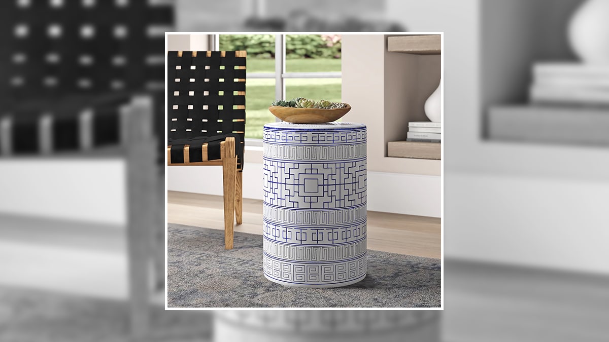 a white garden stool with blue geometrical designs is kept  by the chair in the living room. 