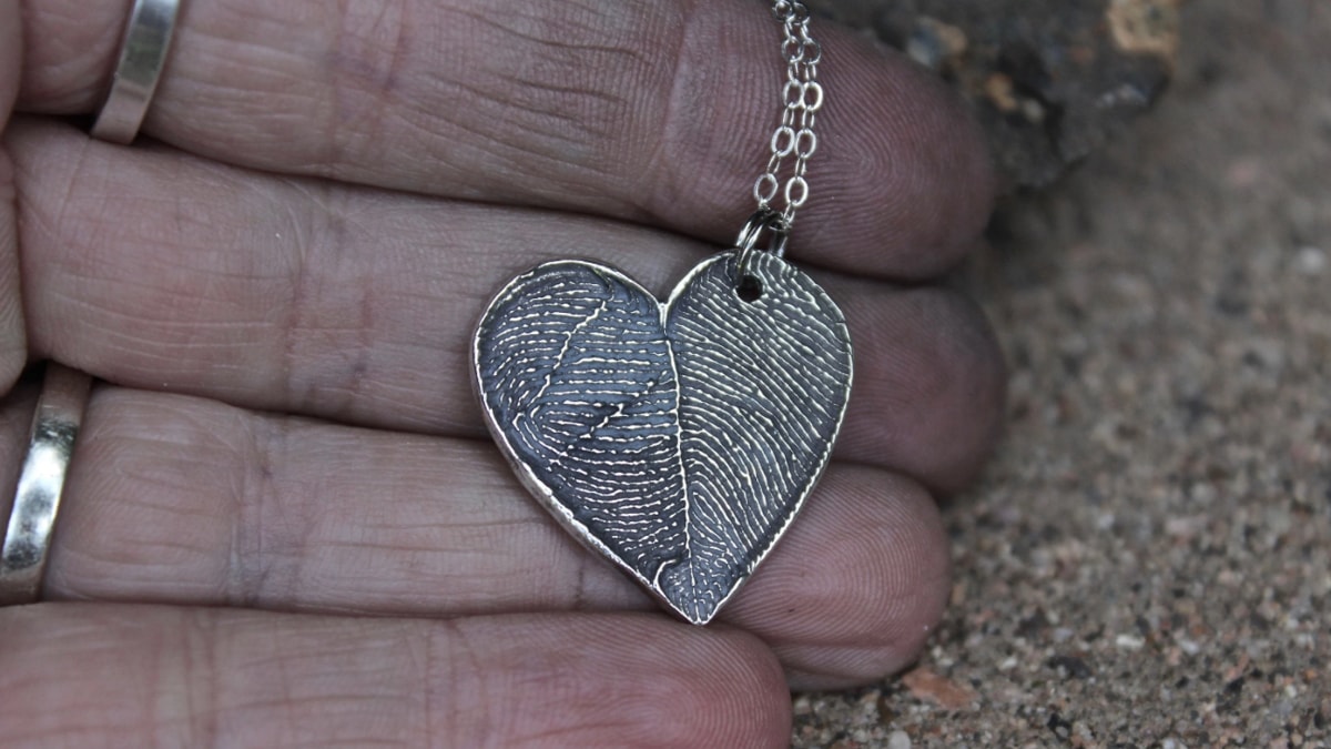 A personalized gift made from two finger prints. Someone is holding it and it is silver in color. This is a graduation gift ideas for granddaughter.