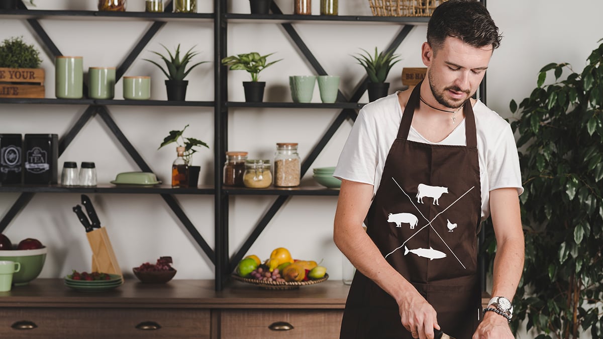 A man wearing a customized apron in the kitchen while making food