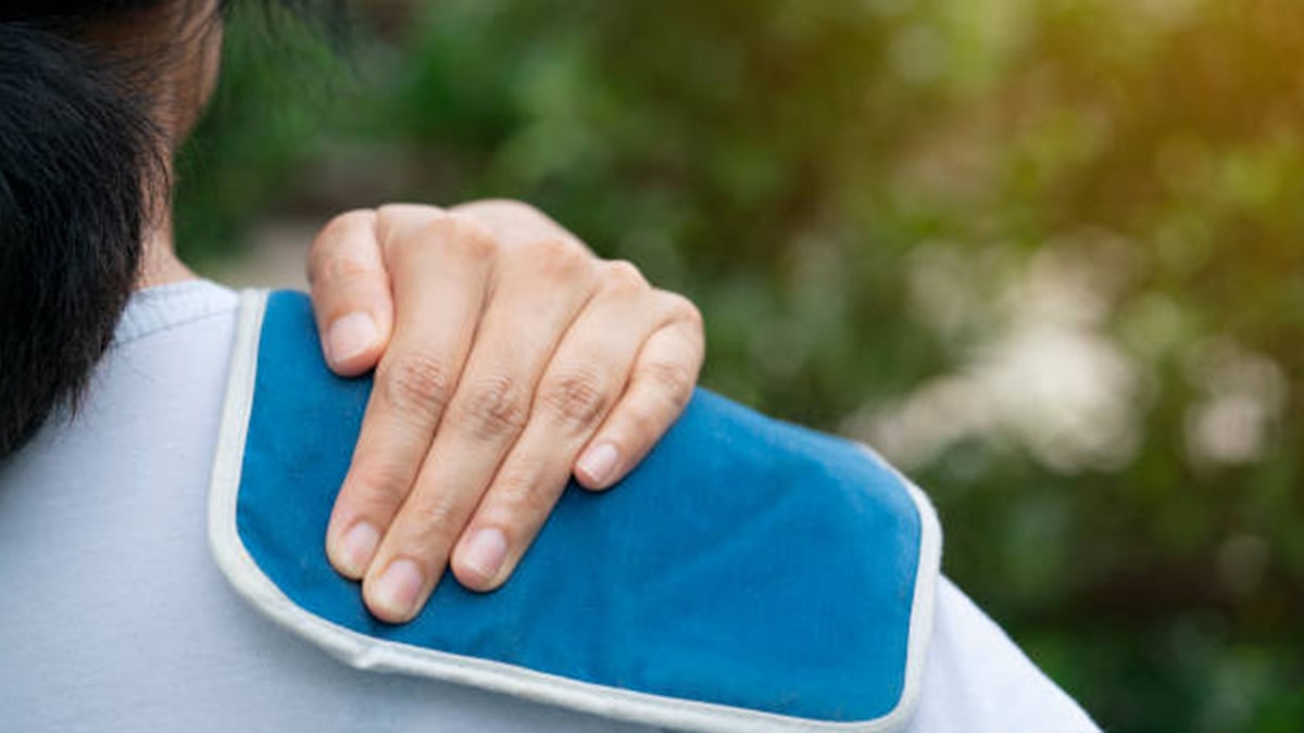 a woman pressing heat pad against her shoulder 