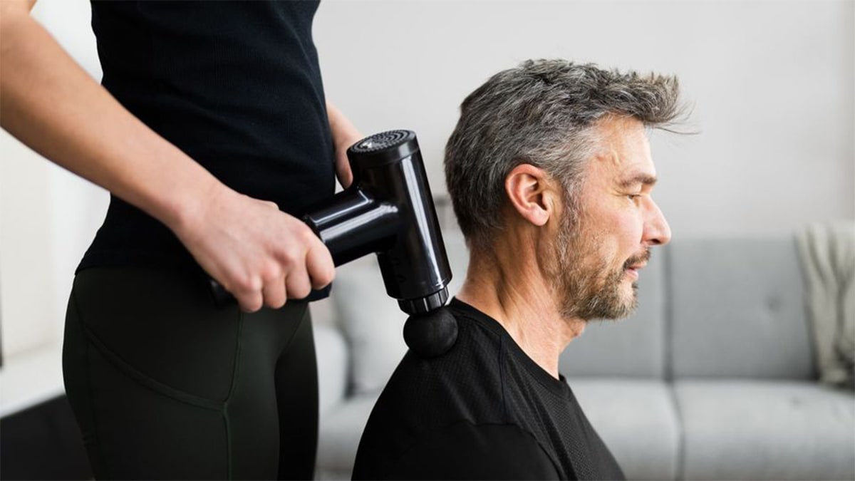 A woman massaging a man's shoulder using a massage gun